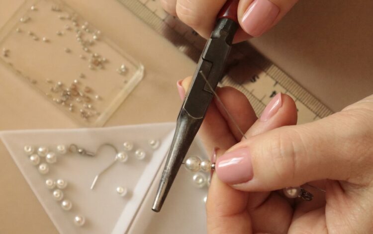 Mains d'une créatrice de bijoux travaillant avec une pince sur une parure de mariage en perles